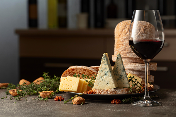 Sfeervolle kaasplank met verschillende kazen, druiven, noten en een glas rode wijn op een houten tafel