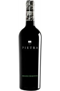 Fles Cantine Menhir Pietra Primitivo 2022 met robijnrood etiket op een houten tafel met wijnaccessoires
