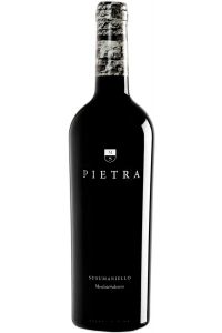 Fles Cantine Menhir Pietra Susumaniello 2023 met robijnrood etiket op een houten tafel met wijnaccessoires